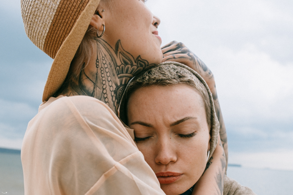 Twee vrouwen omarmen elkaar, waarbij de één de ander troost tijdens een emotioneel moment, een visuele weergave van hoogsensitiviteit en het vermijden van meelijden.