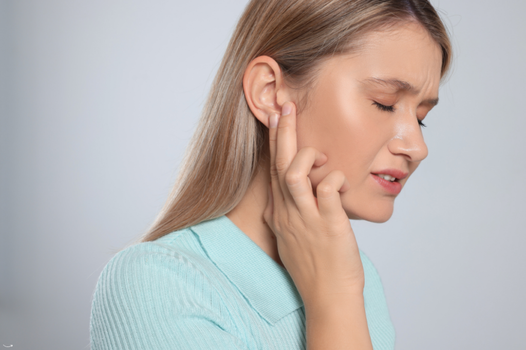 Vrouw met een pijnlijk gezicht die haar hand op haar oor houdt door oorsuizen (tinnitus)