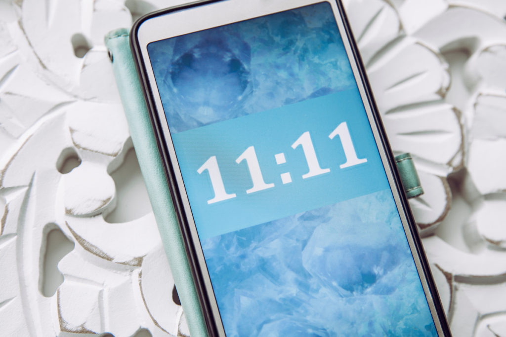 Close-up van een smartphone waarop het tijdstip 11:11 wordt weergegeven op een achtergrond met blauwe kristallen.