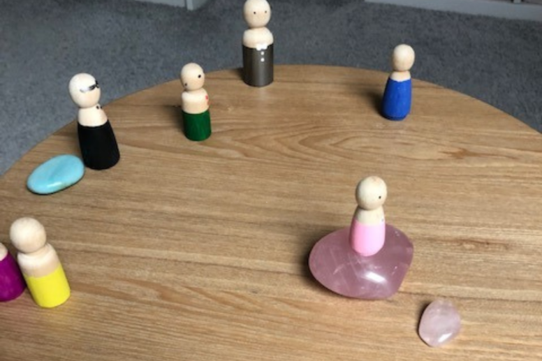 Familieopstelling met houten poppetjes en edelstenen op een houten tafel.