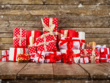 Een verzameling mooi ingepakte cadeautjes in rood en wit, versierd met linten, tegen een houten achtergrond met vallende sneeuwvlokken.