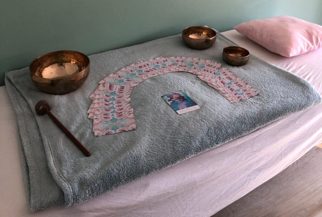 Behandeltafel in holistische praktijk met mintgroene deken, roze kussen, orakelkaarten en klankschalen tegen zachte groene muur