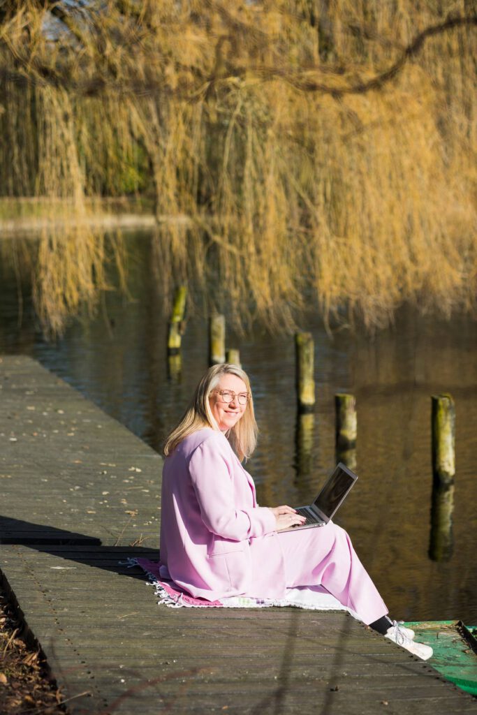 Sandy vivaldi, holistisch therapeut, zittend aan de rand van het water met haar laptop op schoot.