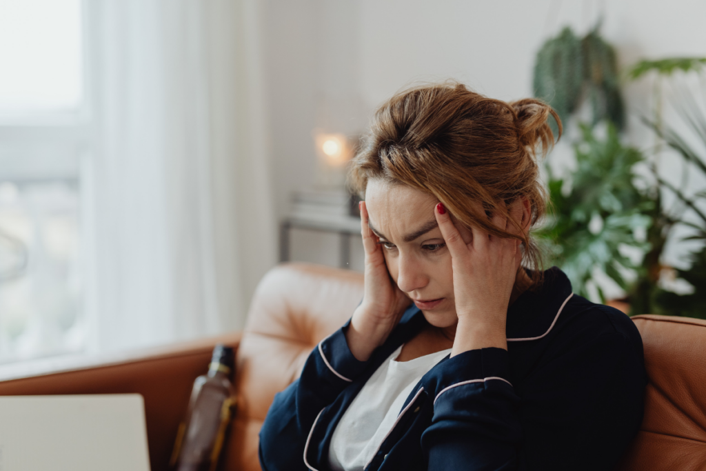 Vrouw zit met hoofdpijn op de bank met haar hoofd in haar handen.