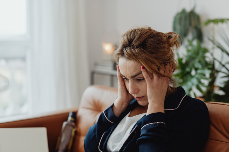 Vrouw zit met hoofdpijn op de bank met haar hoofd in haar handen.