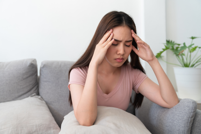 Vrouw zit gestresst op de bank met haar hoofd verslagen in haar handen.