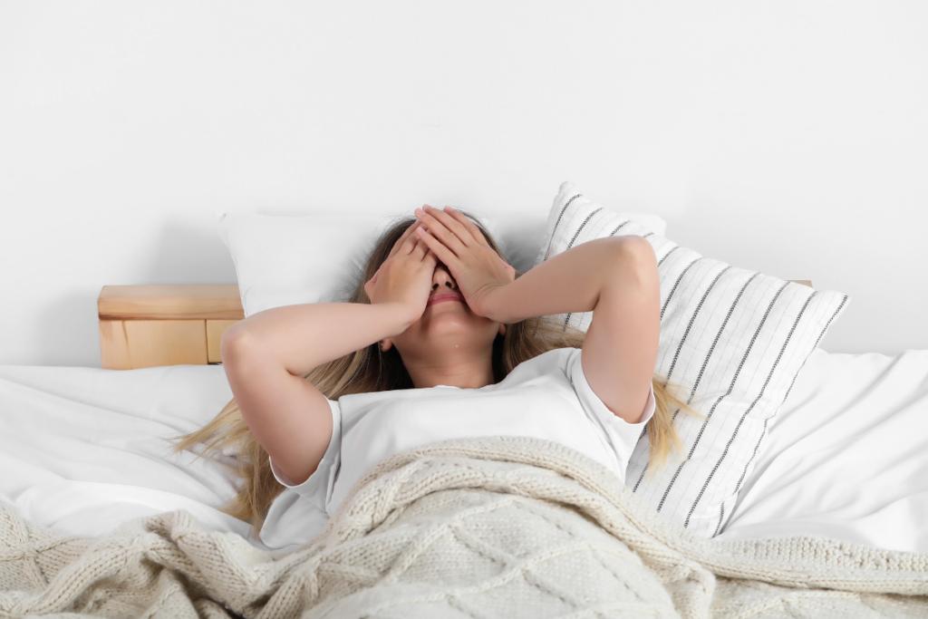 Vrouw ligt onrustig in bed met haar handen over haar ogen.